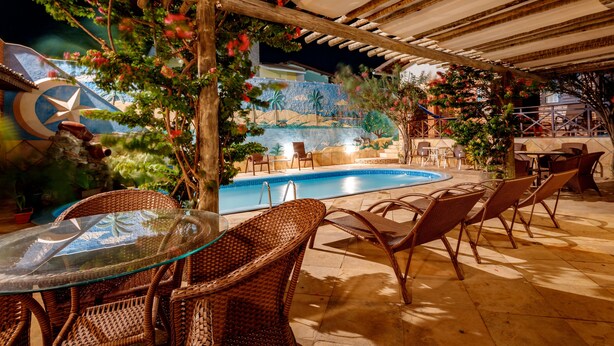 An outdoor pool area with wicker furniture and a glass table. - Pousada Jardim dos Orixás (Aracati)