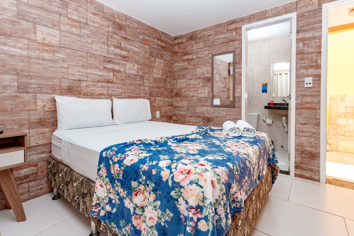 A bedroom with a bed, a nightstand, a mirror, and a bathroom visible through an open door.