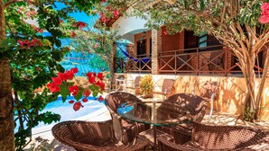 Wicker furniture, a glass table, and a view of a pool and building. - Pousada Jardim dos Orixás (Aracati)