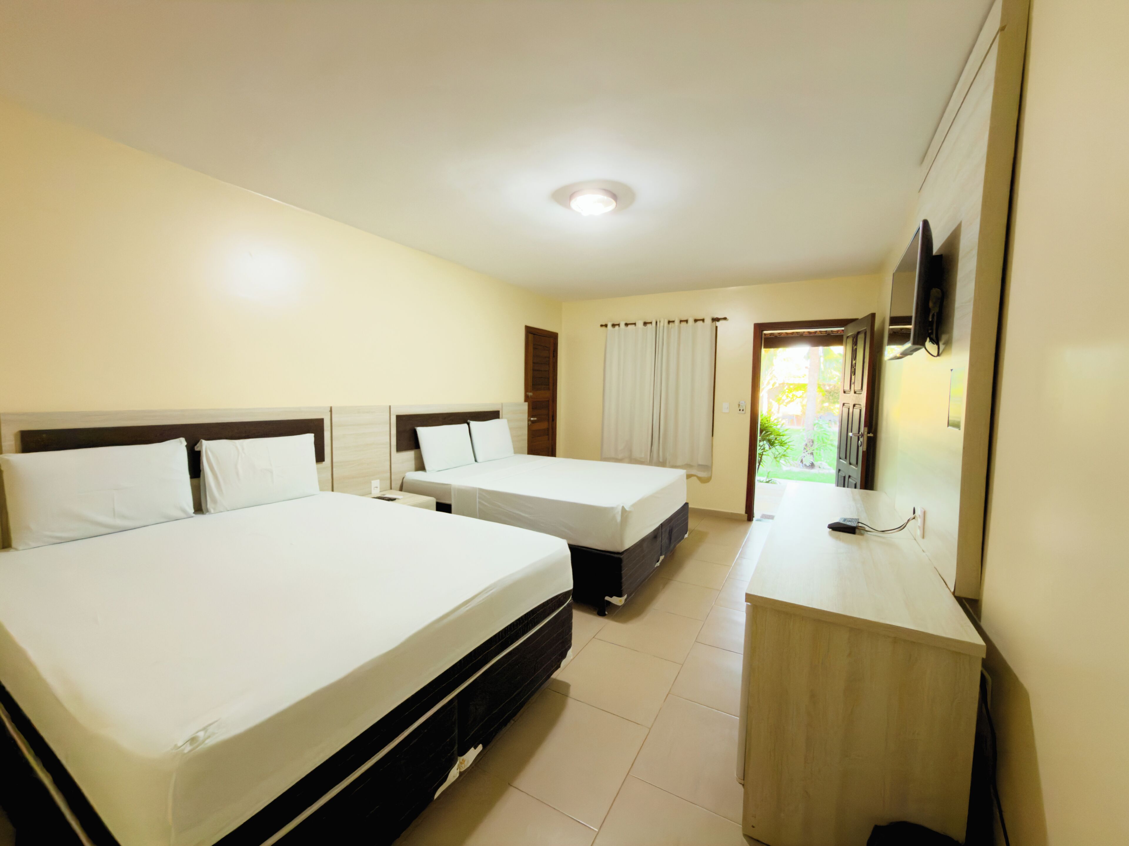 A hotel room with two beds, a desk, a television, and a door leading to a balcony.