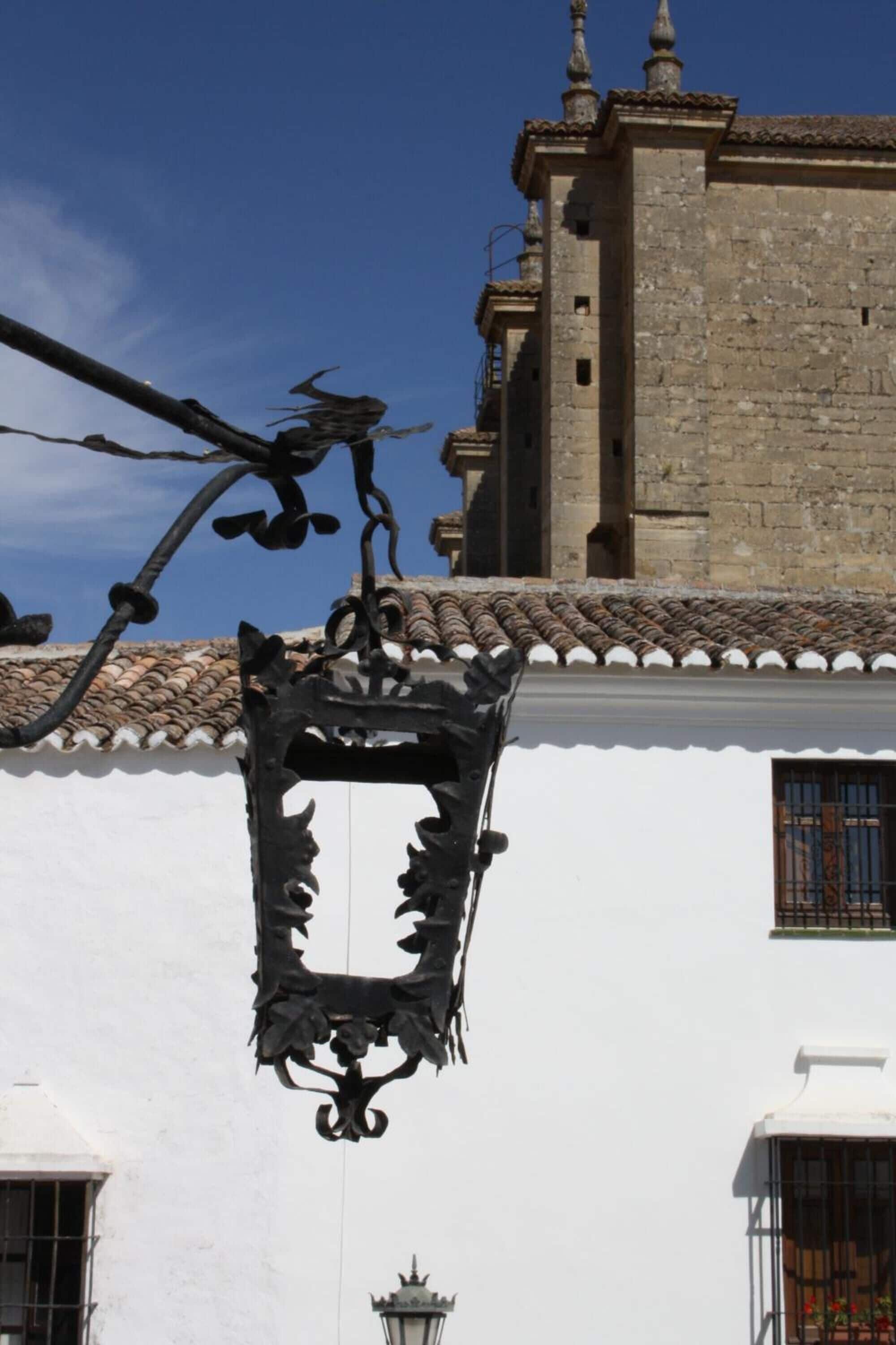 A building with a white facade, a black wrought iron street lamp, and a tiled roof.