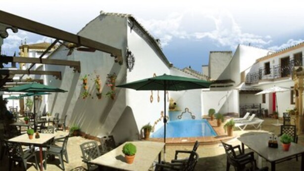 An outdoor patio area with tables and chairs, a swimming pool, and a covered seating area. - Hotel La Ciudad (Ronda)