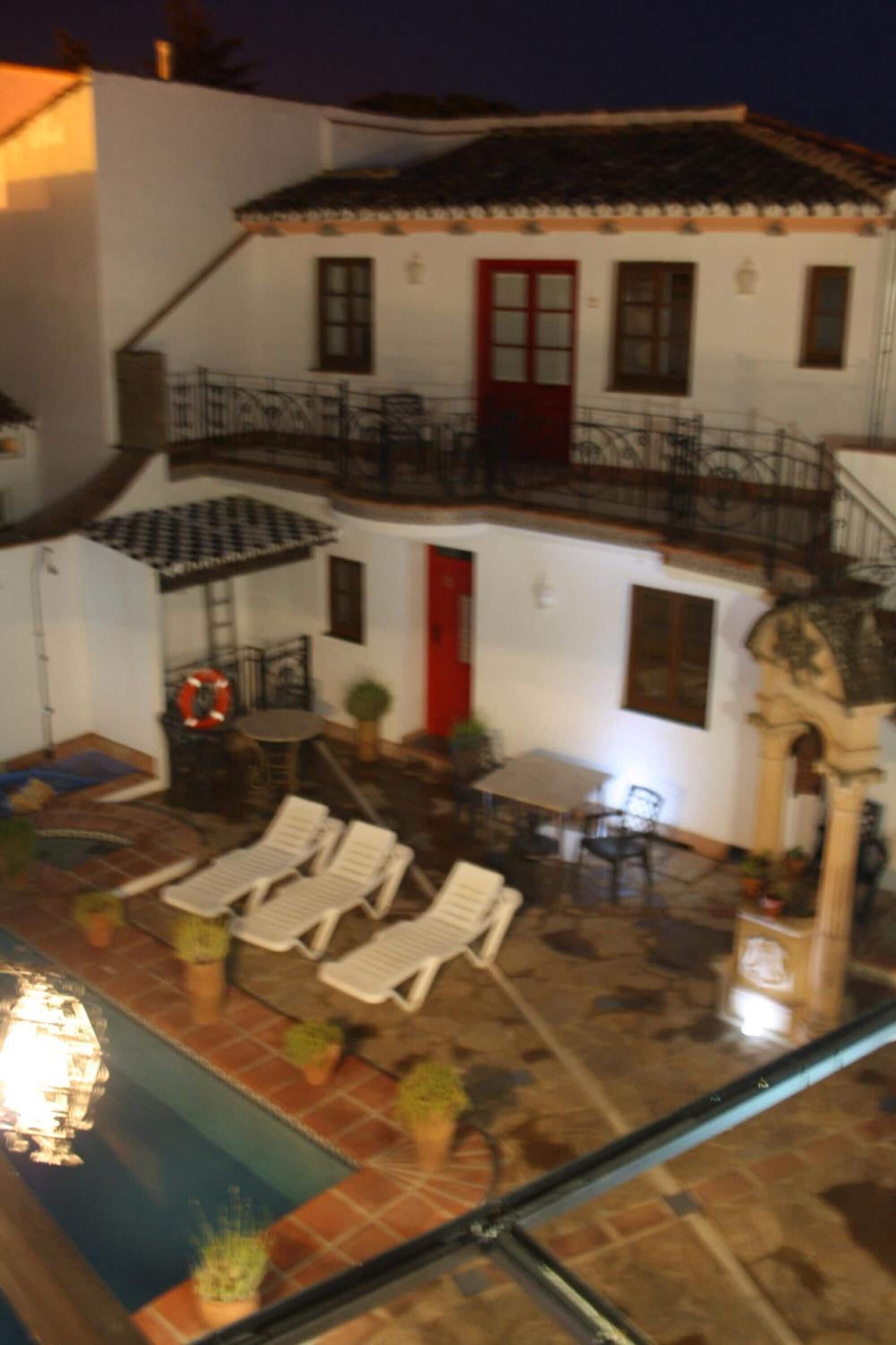 Un edificio de dos pisos con una puerta roja, un balcón y un área de piscina con sillas de descanso.