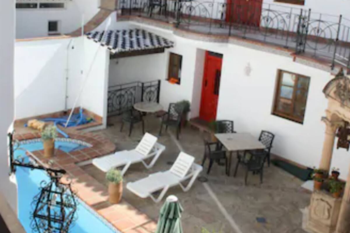 A courtyard with a swimming pool, lounge chairs, and a dining area.