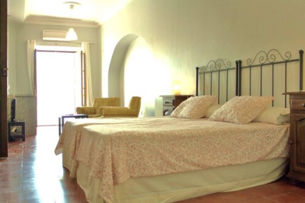 A bedroom with a bed, two bedside tables, a chair, and an arched doorway.