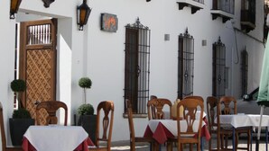 An outdoor seating area with wooden chairs and tables, a white building with balconies, and a cobblestone street. - Hotel La Ciudad (Ronda)