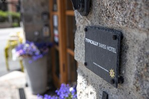 Ein Schild an einer Steinsäule mit der Aufschrift 'TYPICALLY SWISS HOTEL' und einem kleinen Logo darunter.