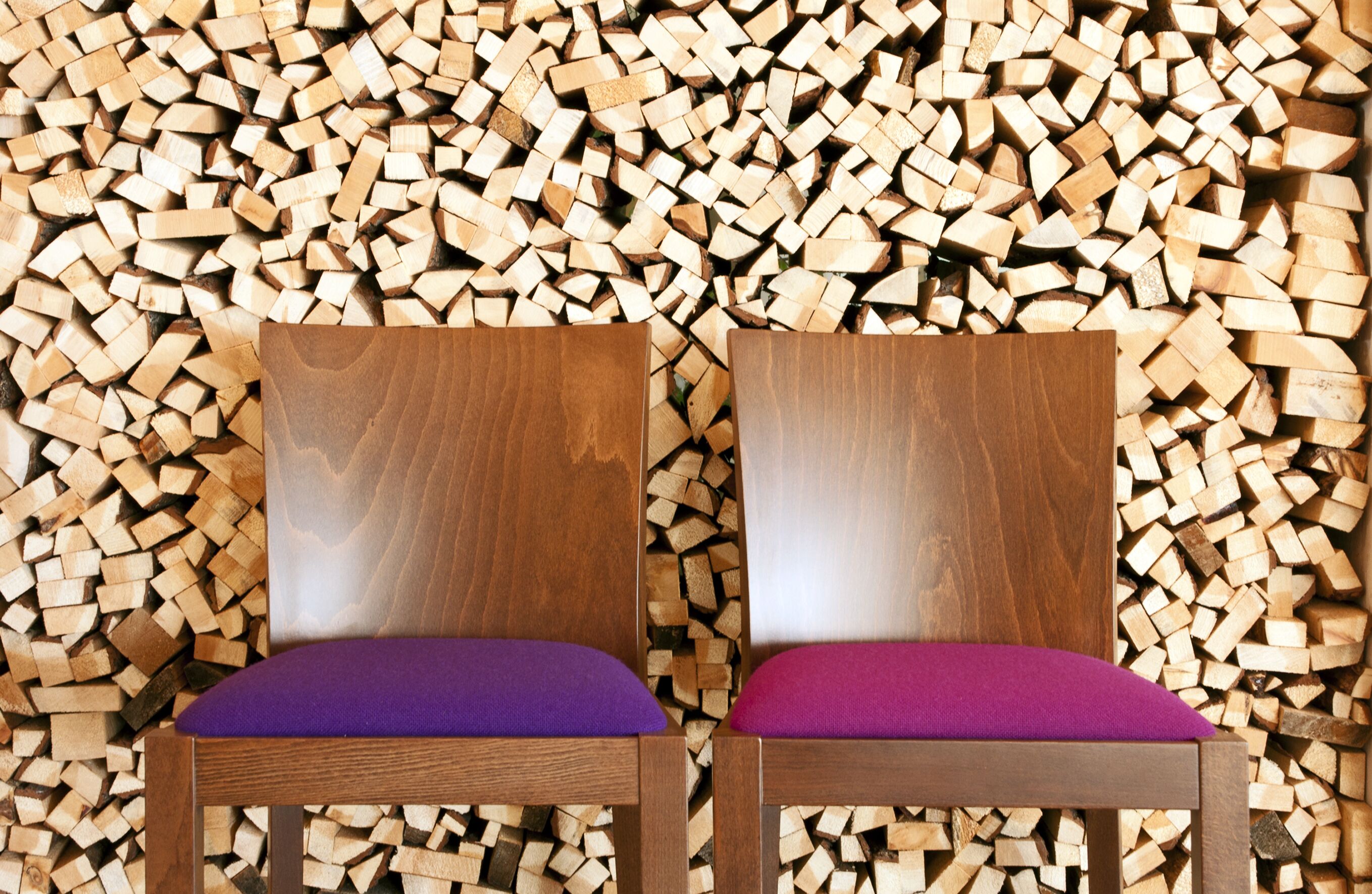 Two wooden chairs with purple cushions against a backdrop of stacked firewood.
