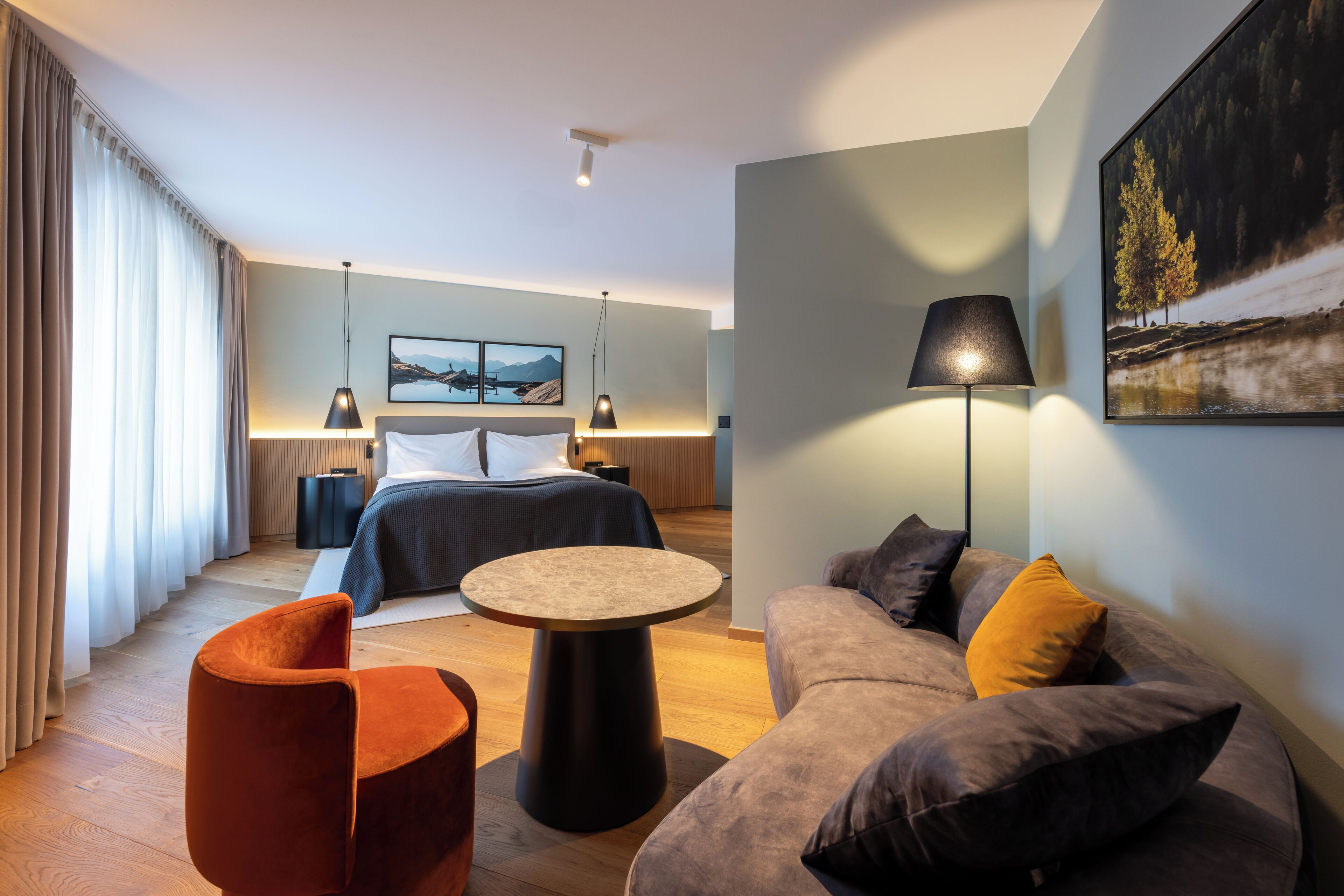Quarto de hotel moderno com uma cama, uma mesa redonda, um sofá e um quadro na parede.