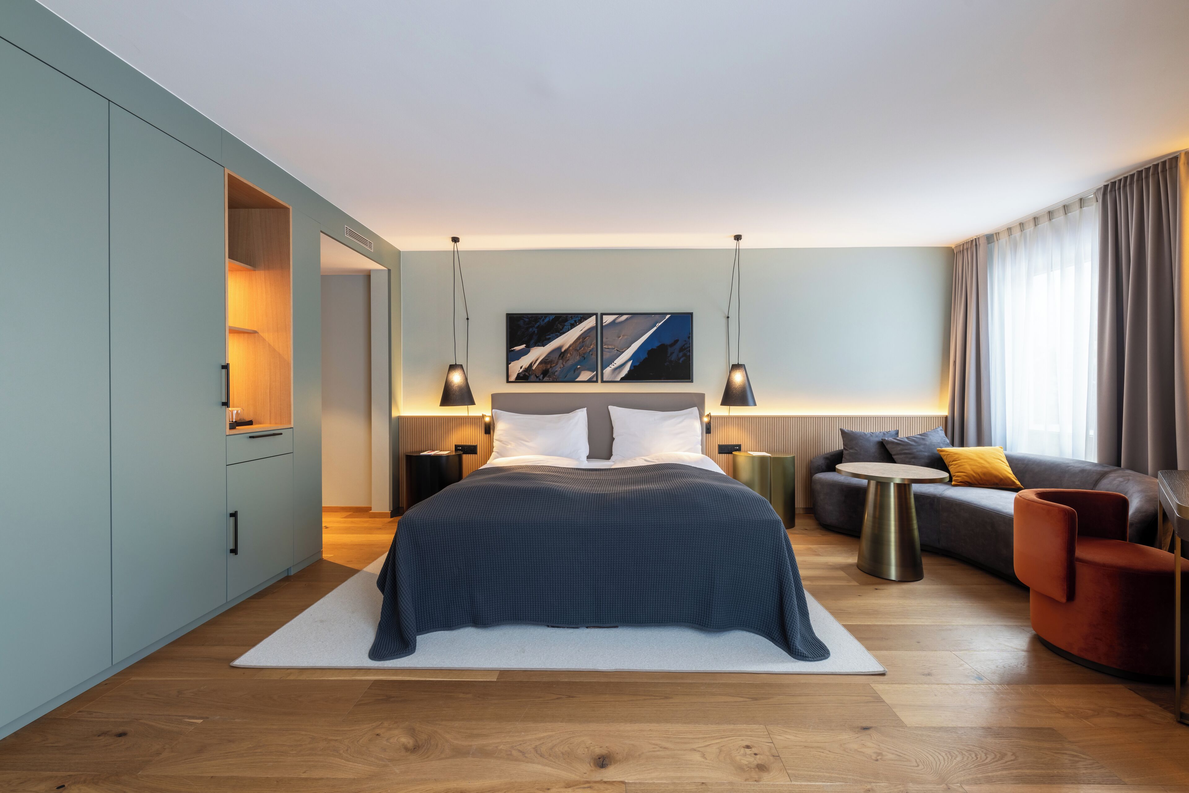 A modern hotel room with a large bed, a sofa, a small round table, and a view of the city.