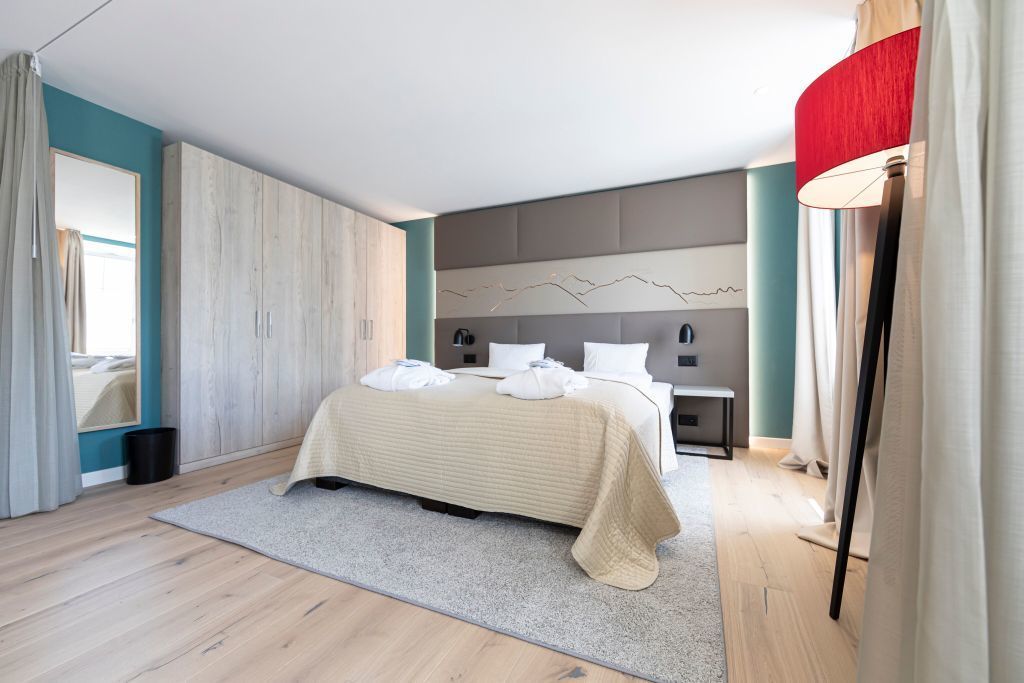 Une chambre moderne avec un grand lit, une table de chevet, une lampe fixée au mur et une vue sur l’extérieur.