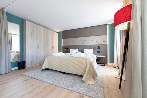 A modern bedroom with a large bed, a nightstand, a wall-mounted lamp, and a view of the outdoors. - Hotel Rosatsch - Stammhaus (Pontresina)