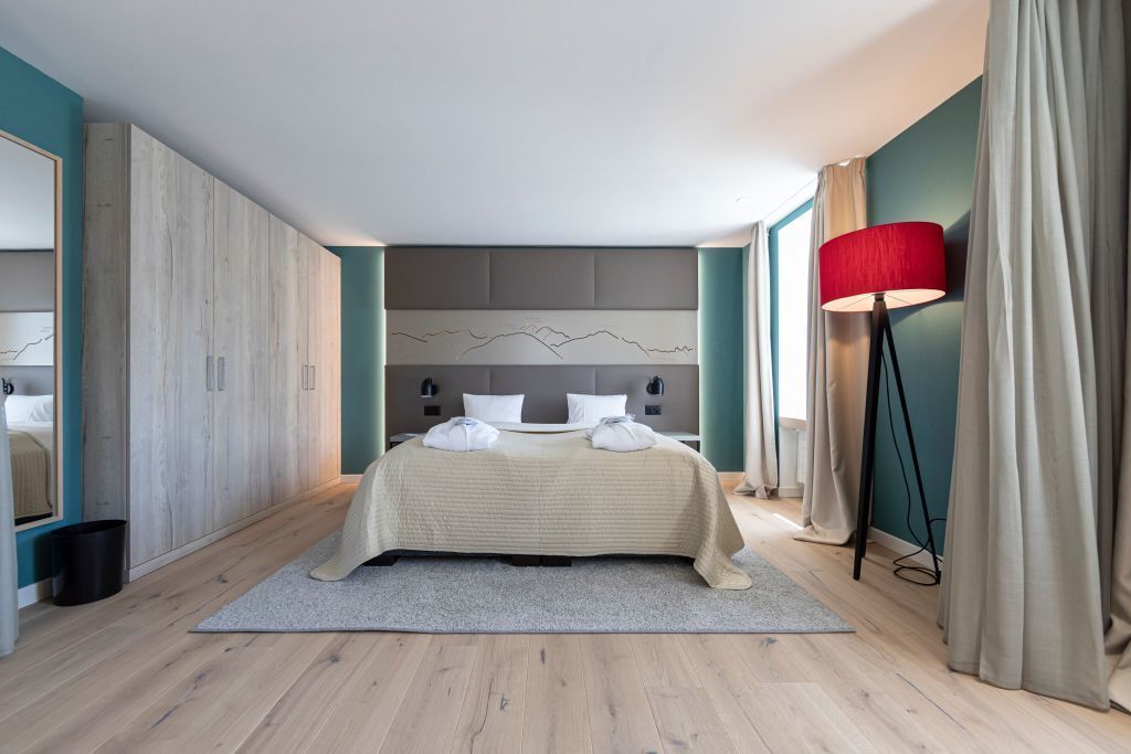 Un dormitorio moderno con una cama grande, un cabecero con diseño de montaña, una lámpara de pie roja y vistas a la ciudad a través de la ventana.