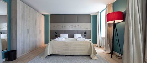 Un dormitorio moderno con una cama grande, un cabecero con diseño de montaña, una lámpara de pie roja y vistas a la ciudad a través de la ventana.