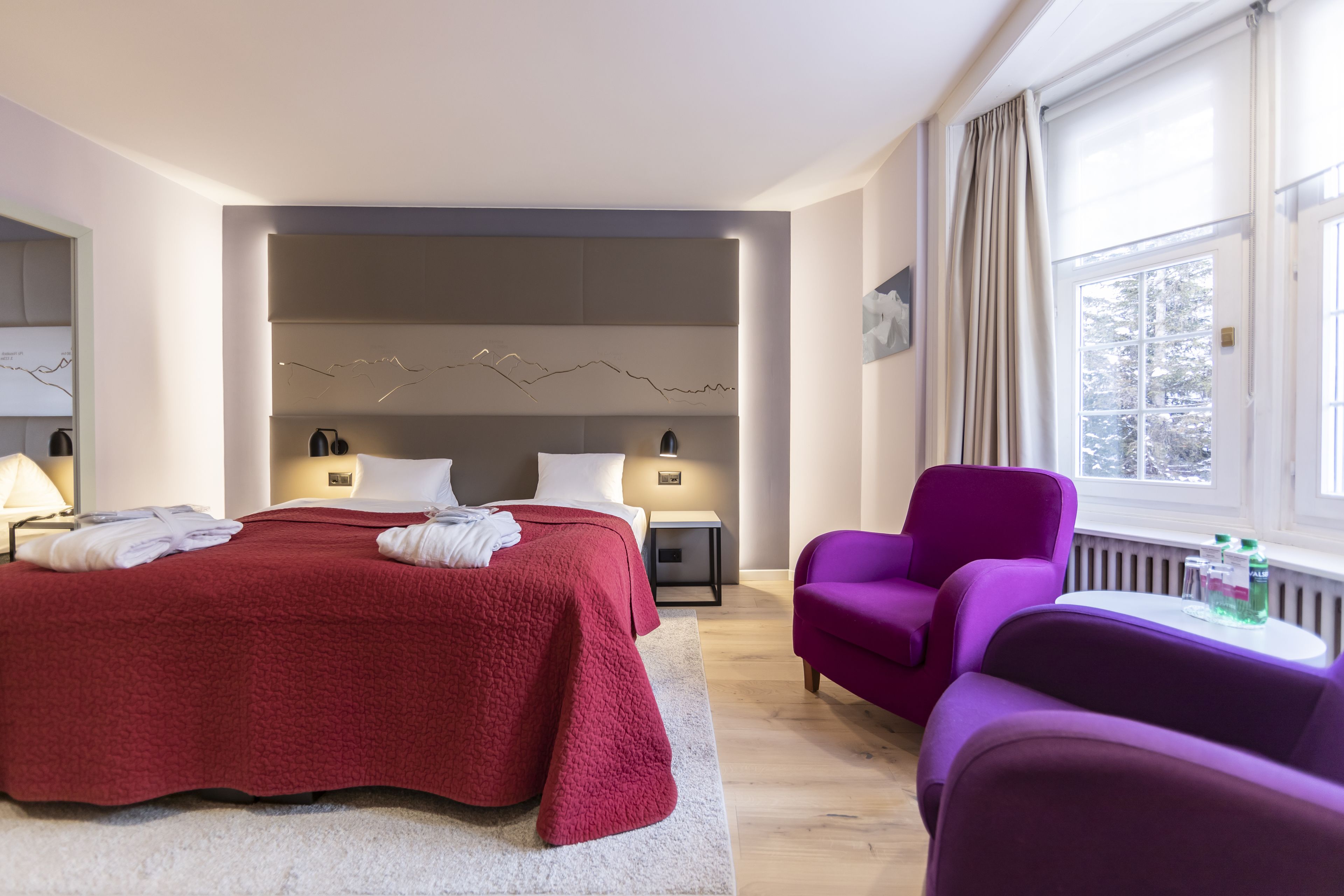 Et moderne hotelværelse med en stor seng, to sengeborde, en lilla lænestol og udsigt til det fri gennem et vindue.