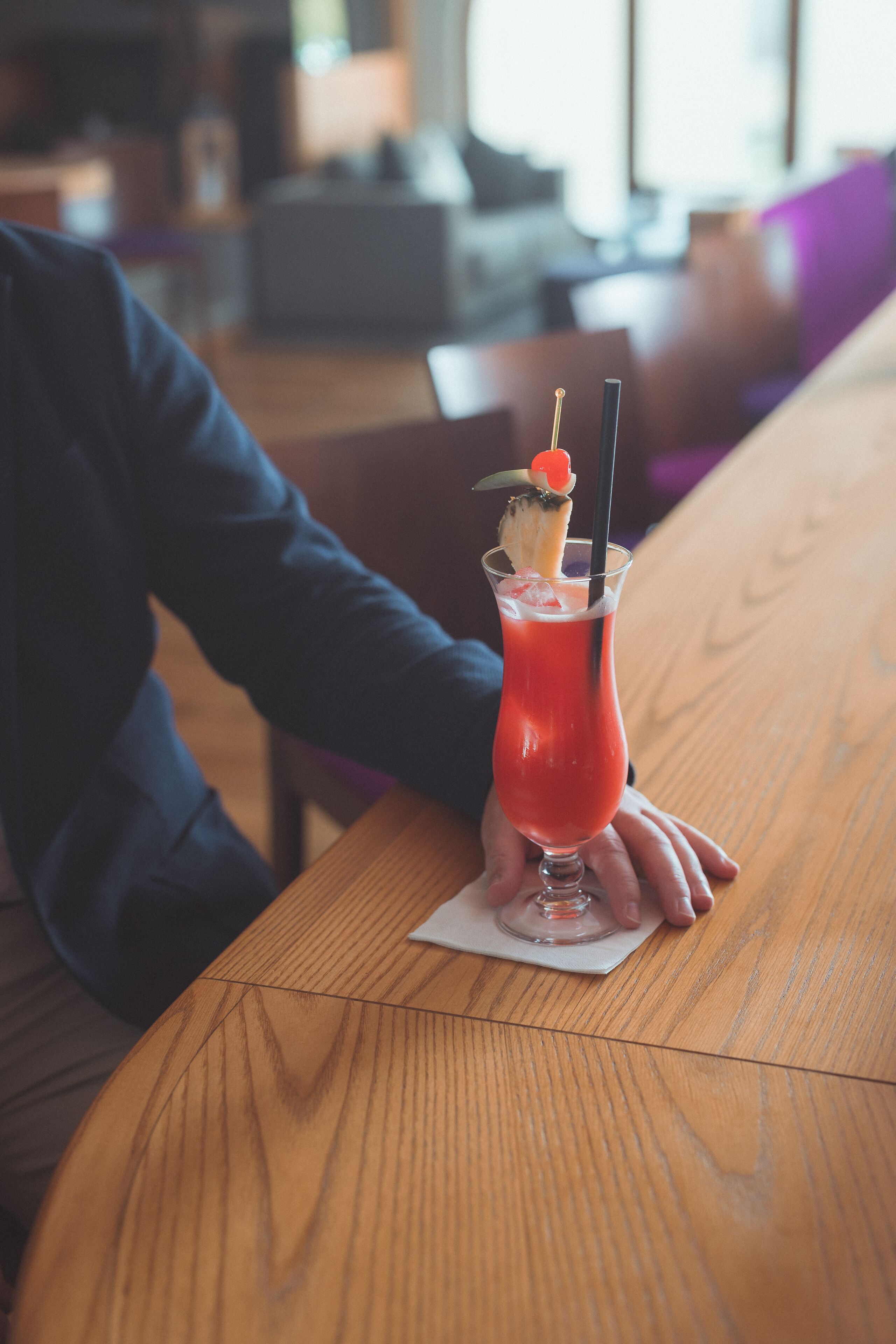 Una mesa de madera con una bebida en un vaso, adornada con una cereza y una pajita.