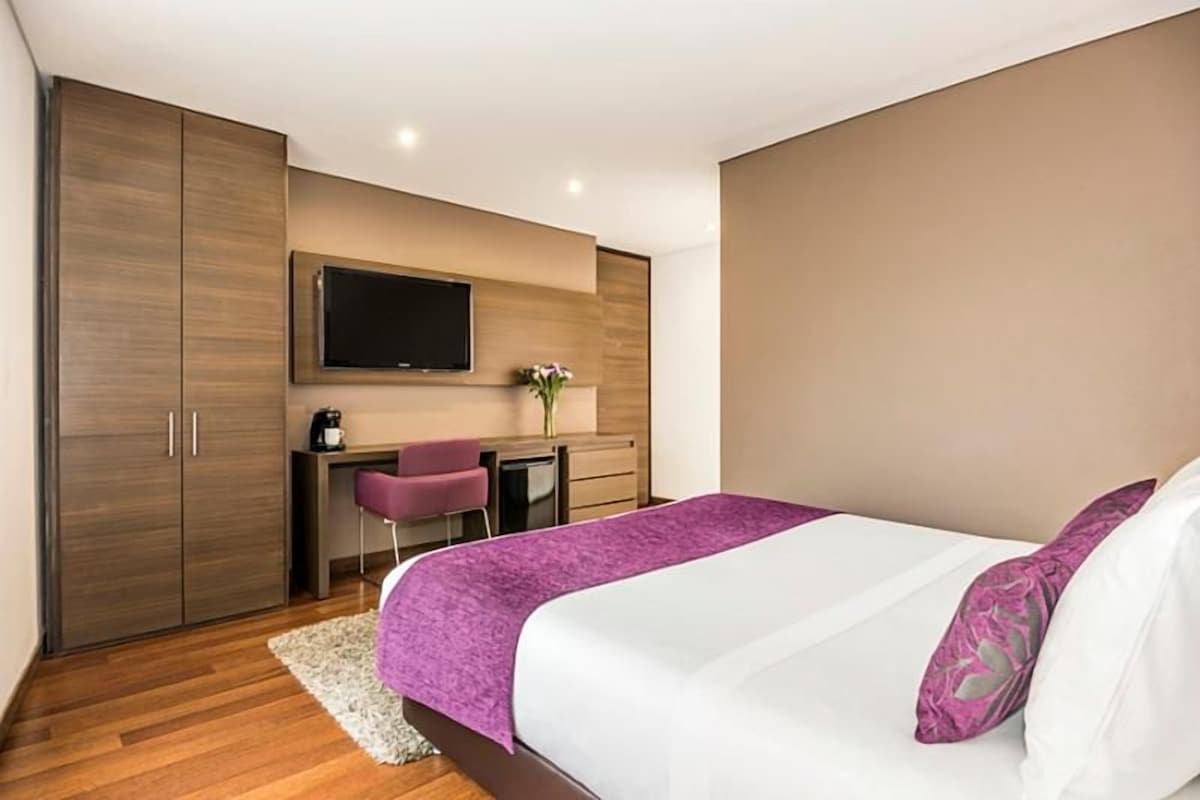 Ein Schlafzimmer mit einem Bett, einem Schreibtisch, einem Stuhl, einem Fernseher und einem Kleiderschrank.
