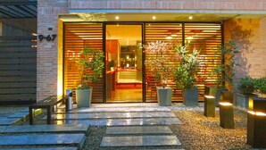 A modern building entrance with a glass door, potted plants, and a stone pathway leading to the entrance. - 84 DC Bogotá By OxoHotel (Bogotá)