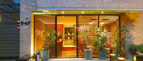 Una entrada moderna de edificio con puerta de vidrio, plantas en macetas y un sendero de piedra que conduce a la entrada.