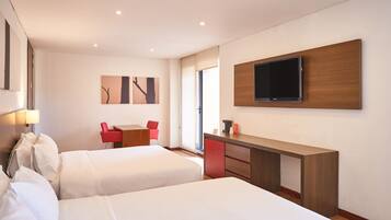 A hotel room with two beds, a desk, a TV mounted on the wall, and a red chair.