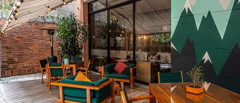 An outdoor patio with wooden furniture, a brick wall, and a mountain mural.