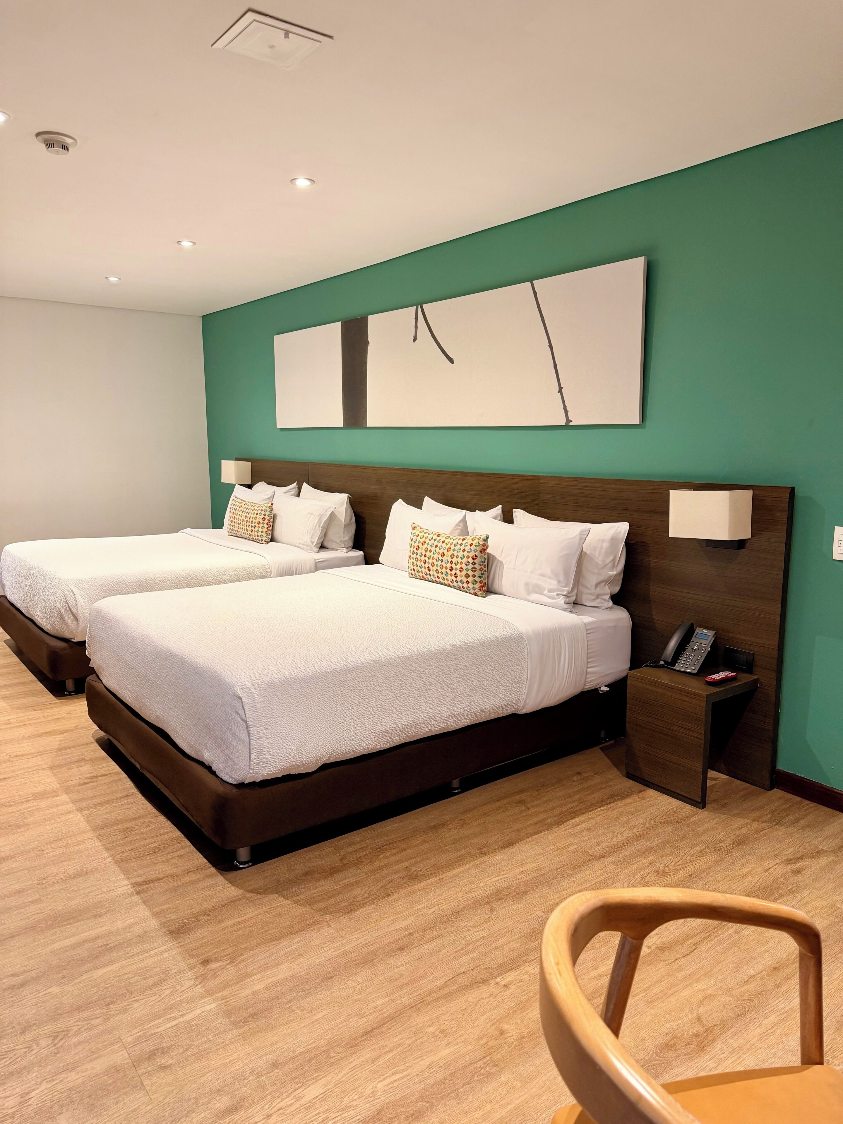 Habitació d'hotel amb dos llits, un sòl de fusta, una paret verda decorativa, un quadre abstracte gran i un telèfon al costat del llit.