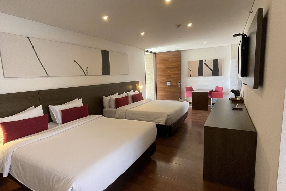 A hotel room with two beds, a desk, a TV, and a sliding door leading to a bathroom.