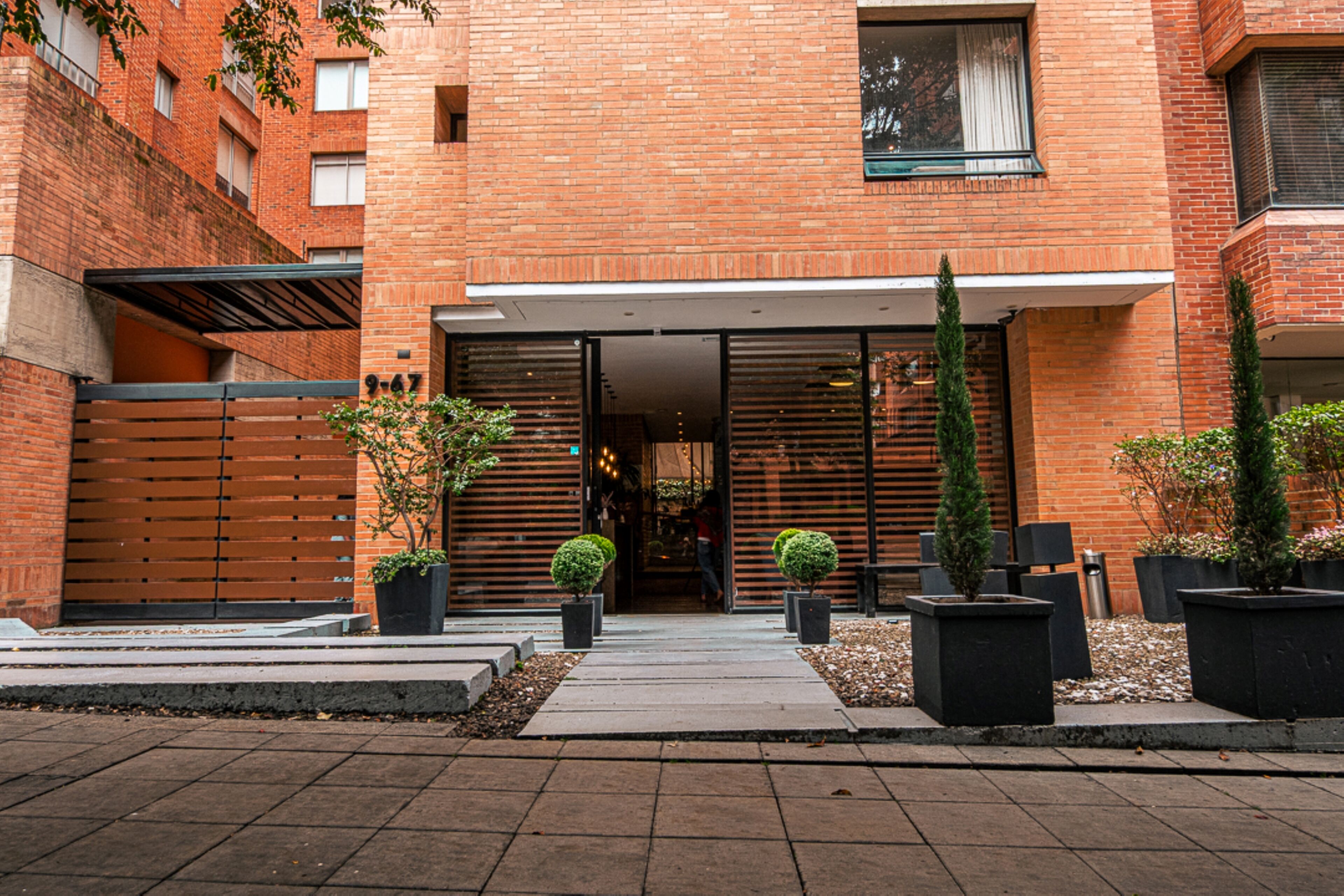 A brick building with a modern entrance, potted plants, and a clear pathway leading to the entrance.