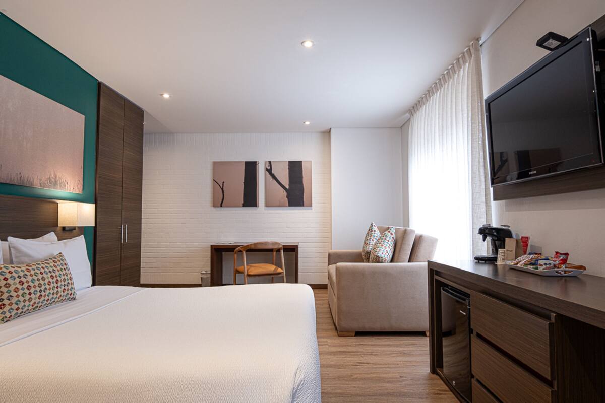 A hotel room with a large bed, a desk, a chair, a sofa, a TV, and a coffee maker.