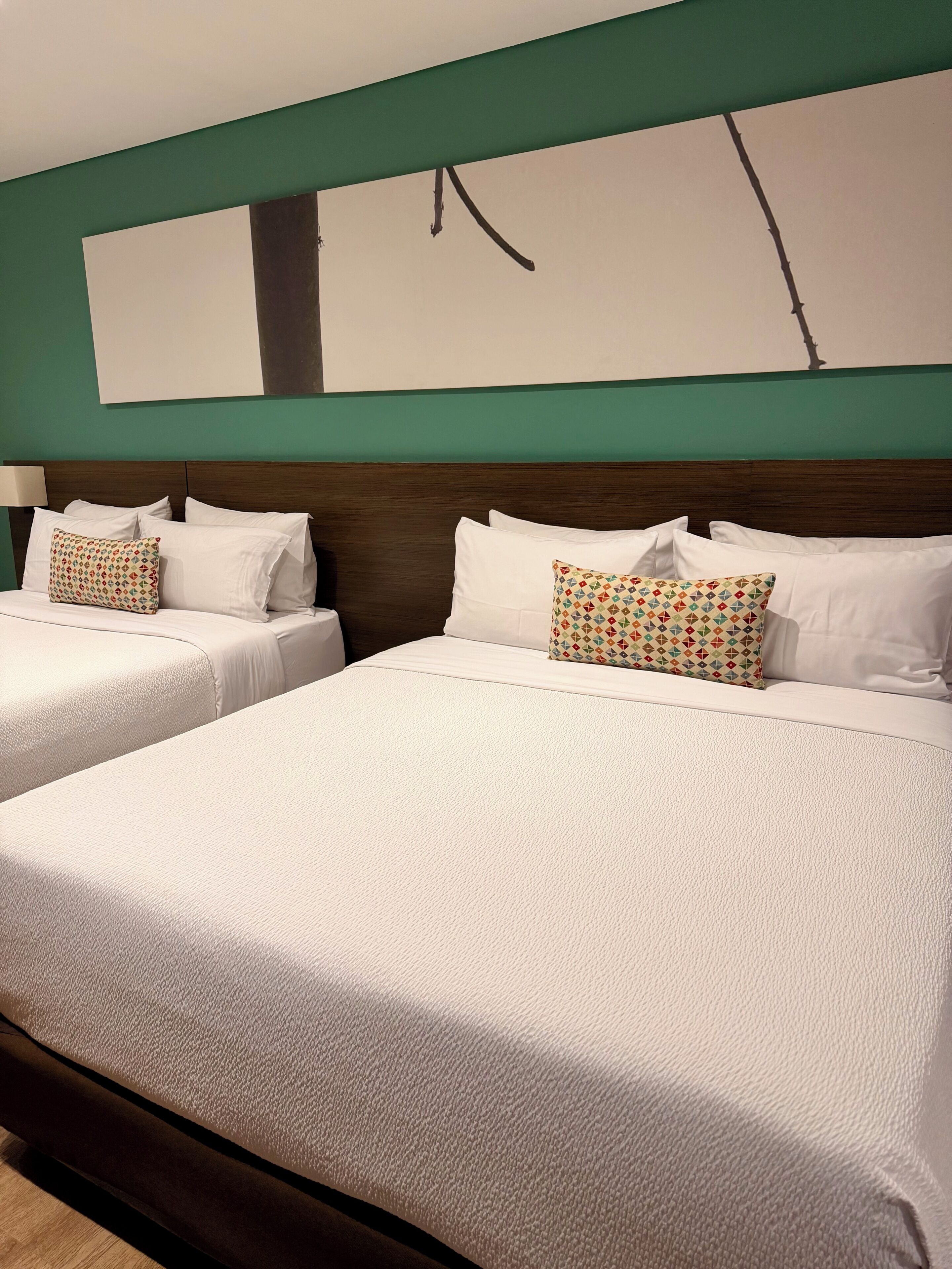 A hotel room with two beds, a green wall, and a large abstract painting.