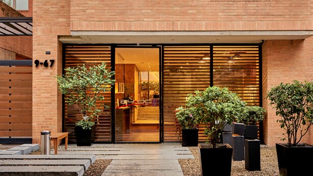 A modern building with a brick facade, large sliding glass doors, and potted plants in the entrance area. - 84 DC Bogotá By OxoHotel (Bogotá)