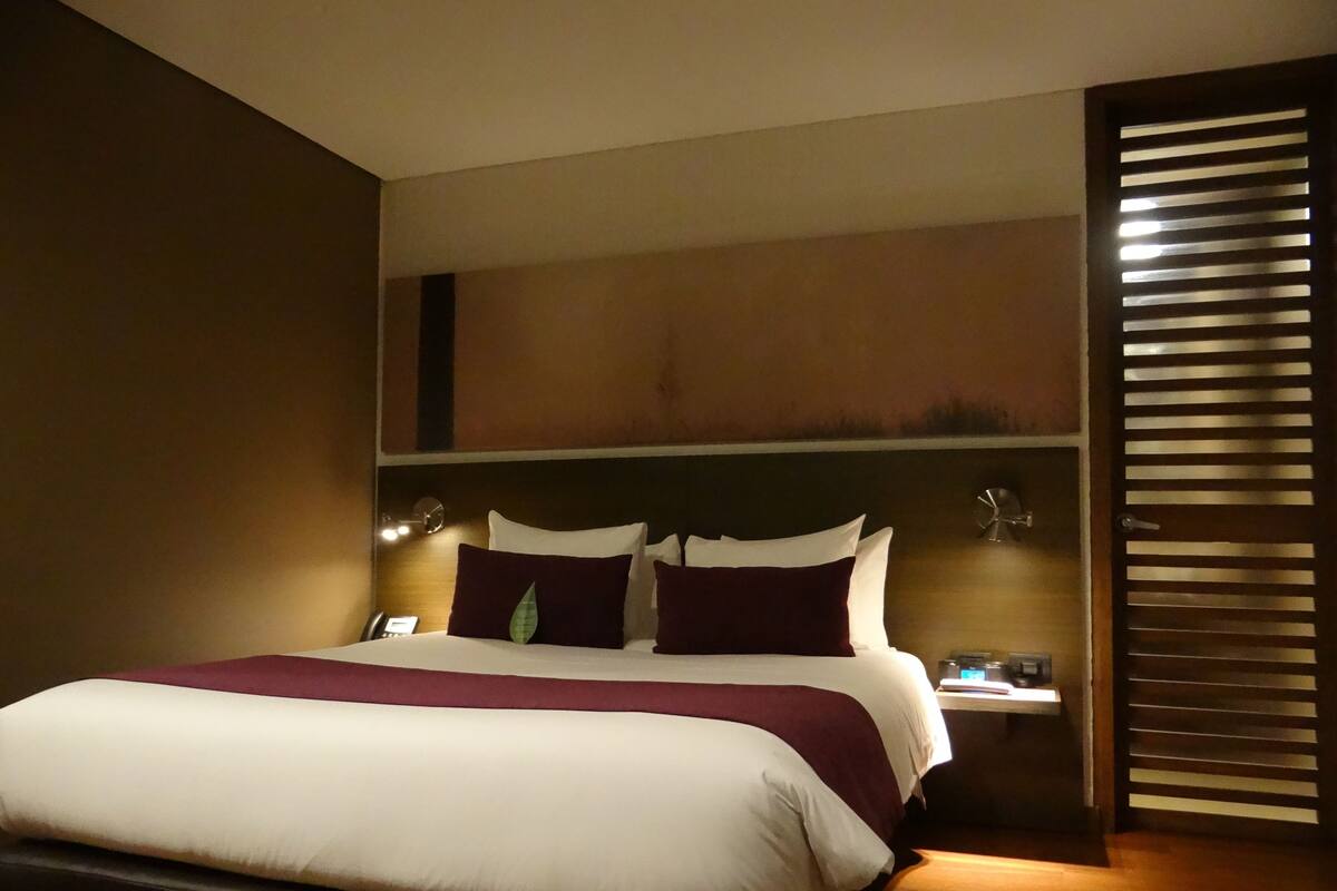 A hotel room with a large bed, bedside tables, a clock, and a window with blinds.