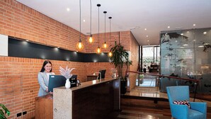 A reception area with a brick wall, a reception desk, a blue chair, and hanging pendant lights. - 84 DC Bogotá By OxoHotel (Bogotá)
