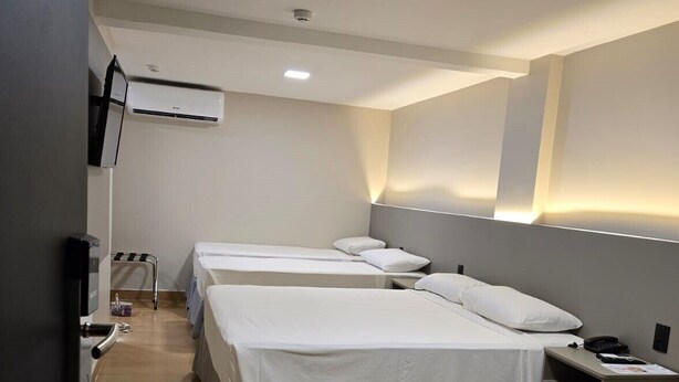 A hotel room with three single beds, a small desk with a chair, a flat-screen TV, and a wall-mounted air conditioning unit. - Hotel Village (Foz do Iguaçu)