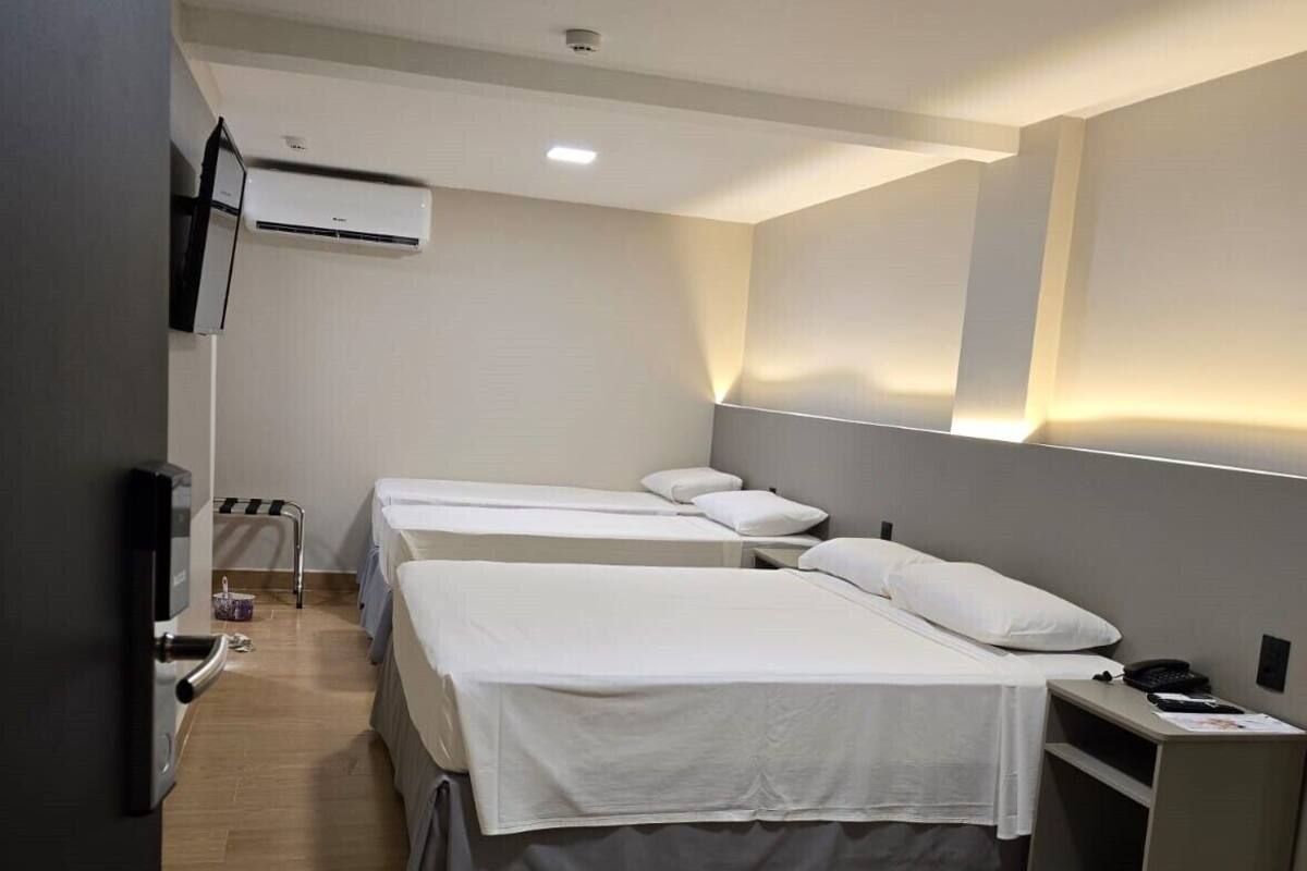 Ein Hotelzimmer mit drei Einzelbetten, einem kleinen Schreibtisch mit Stuhl, einem Flachbildfernseher und einer Wandklimaanlage.