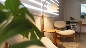 A modern living room with a wooden chair, a floor lamp, and a bookshelf with plants. - Hotel Village (Foz do Iguaçu)