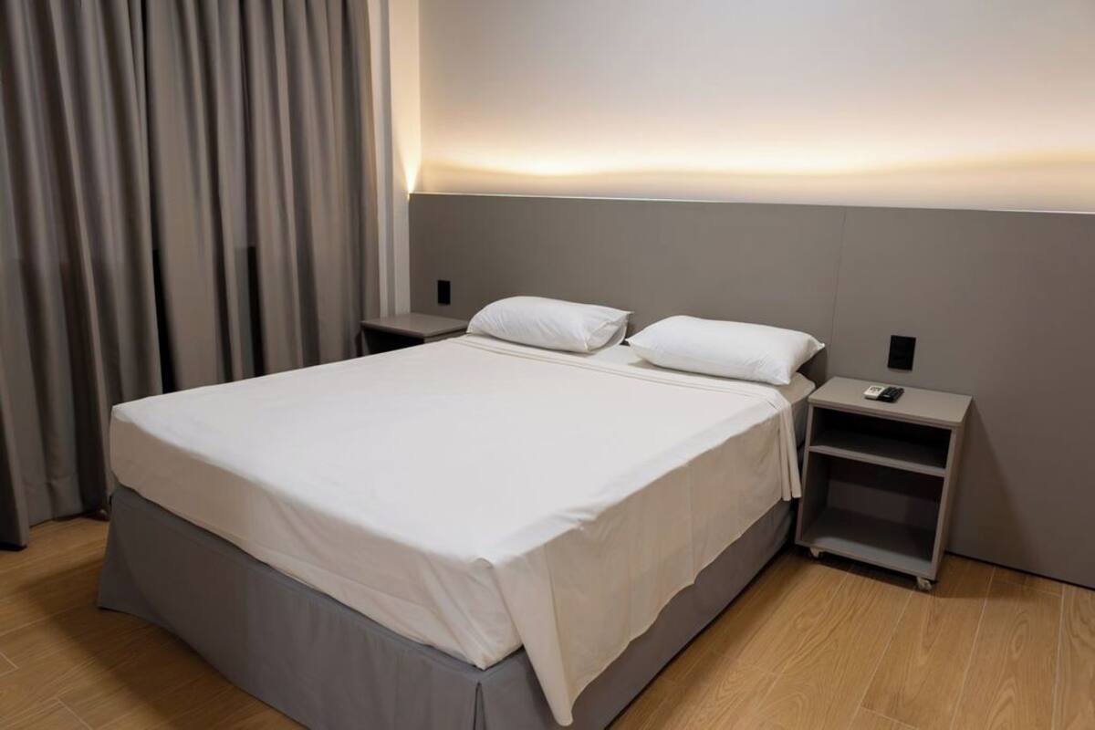 Ein modernes Hotelzimmer mit einem großen Bett, einem Nachttisch mit Lampe und einem kleinen Tisch.