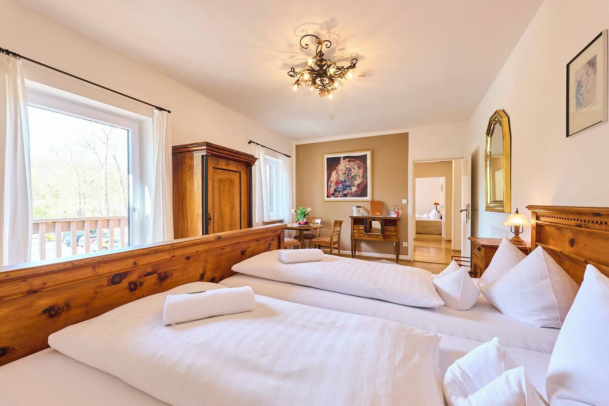 Habitación de hotel con dos camas, un armario de madera, un escritorio con una silla, una lámpara de escritorio, un espejo y un cuadro en la pared.