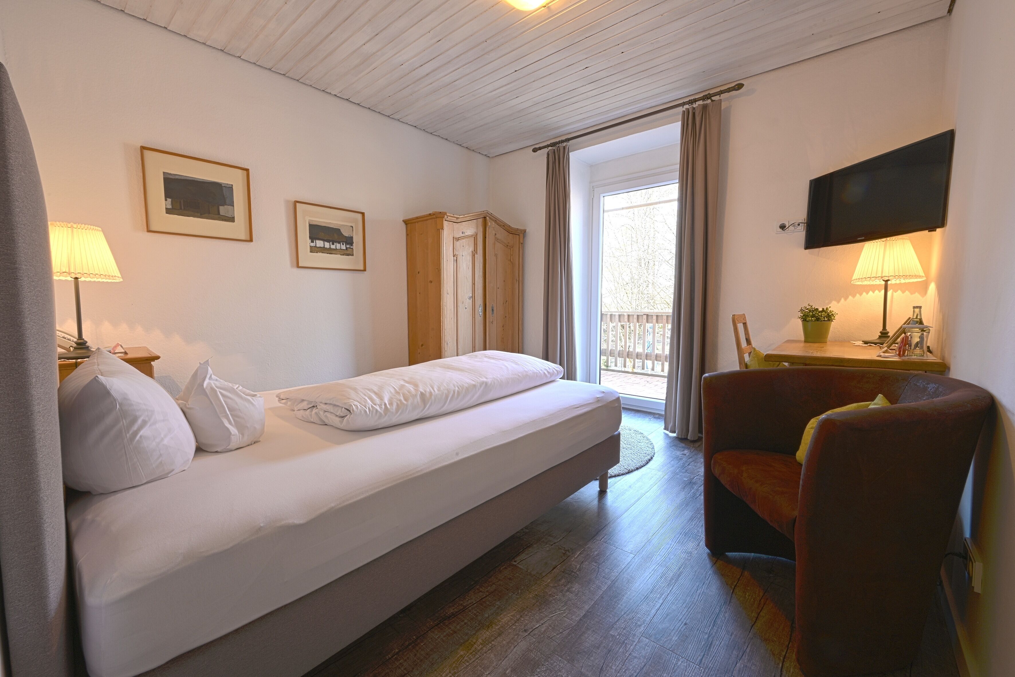 A hotel room with a bed, a chair, a TV, and a window with curtains.