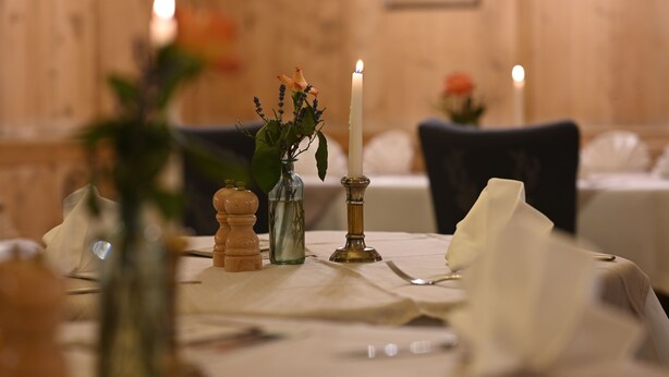 Una mesa dispuesta con mantel blanco, una vela encendida, salero y pimentero, y un jarrón con flores.
