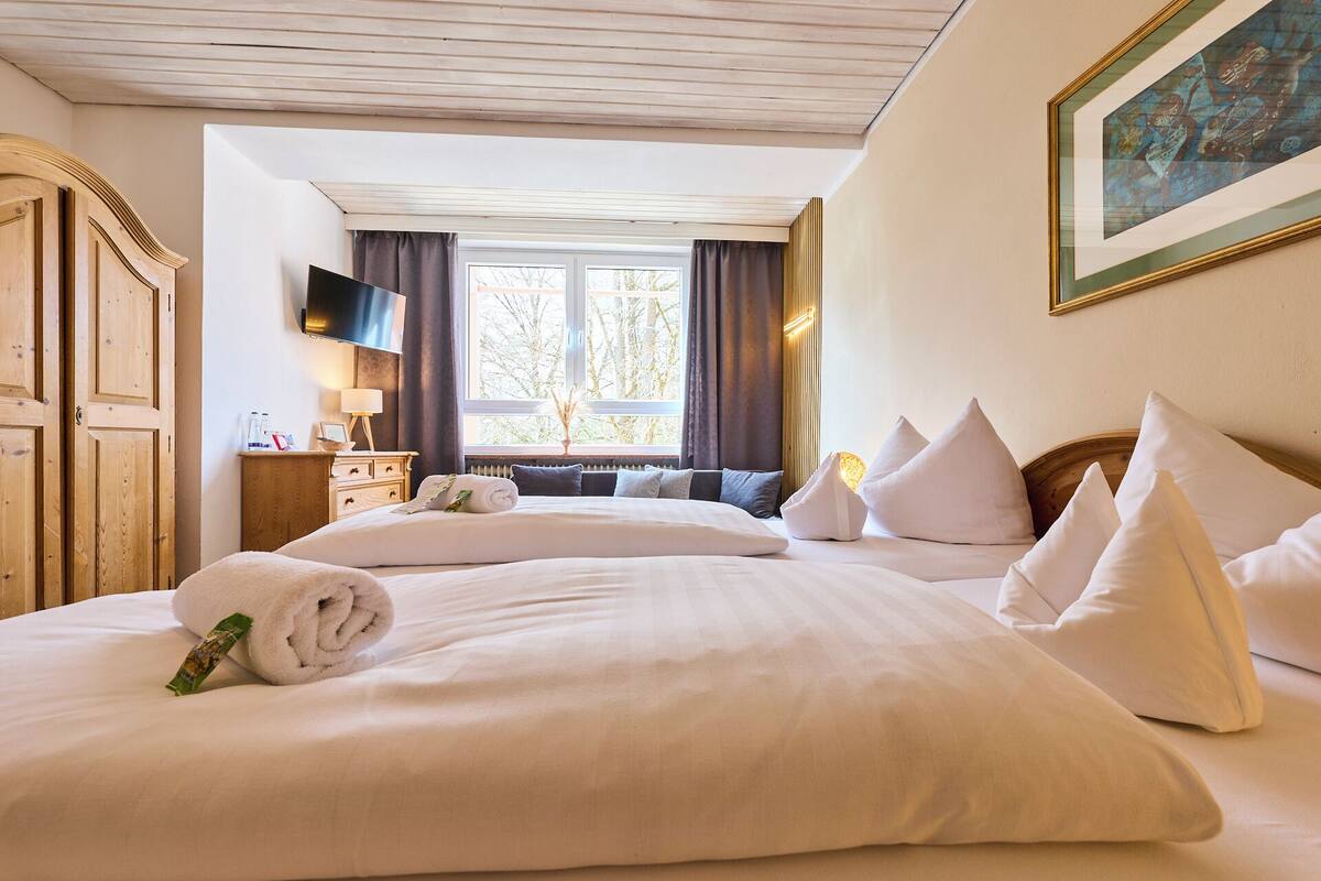 Habitación de hotel con dos camas, un armario de madera, un televisor y una ventana con cortinas.
