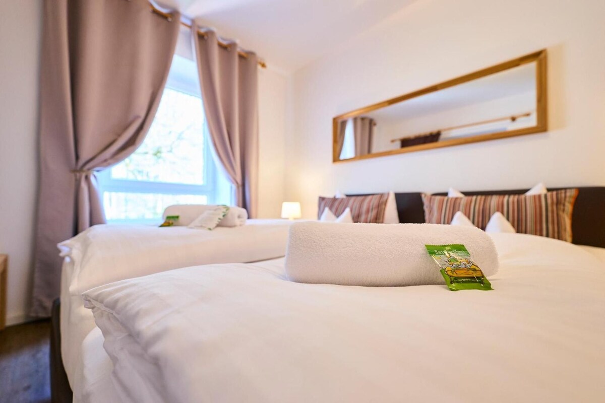 A hotel room with two beds, a window with curtains, a bedside lamp, and a green object on one bed.