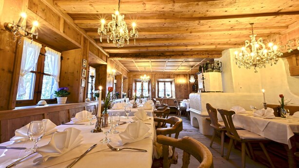 Ein Holzeinrichtung mit Chandeliern, gedeckten Tischen und fensterartigen Öffnungen mit Vorhängen.