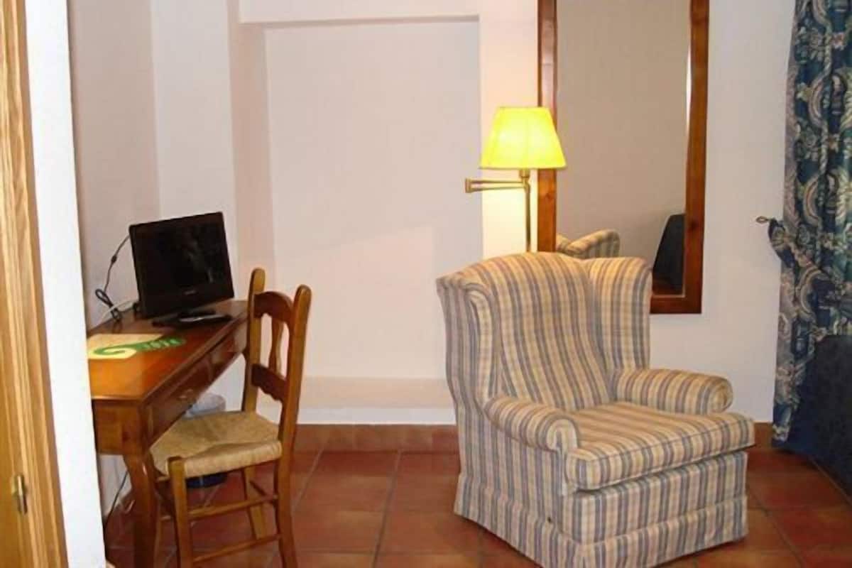 A room with a striped armchair, a wooden desk with a computer, a lamp, and a mirror on the wall.