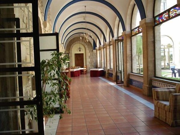 A spacious hall with a high arched ceiling, a central chandelier, and a large window on the right.