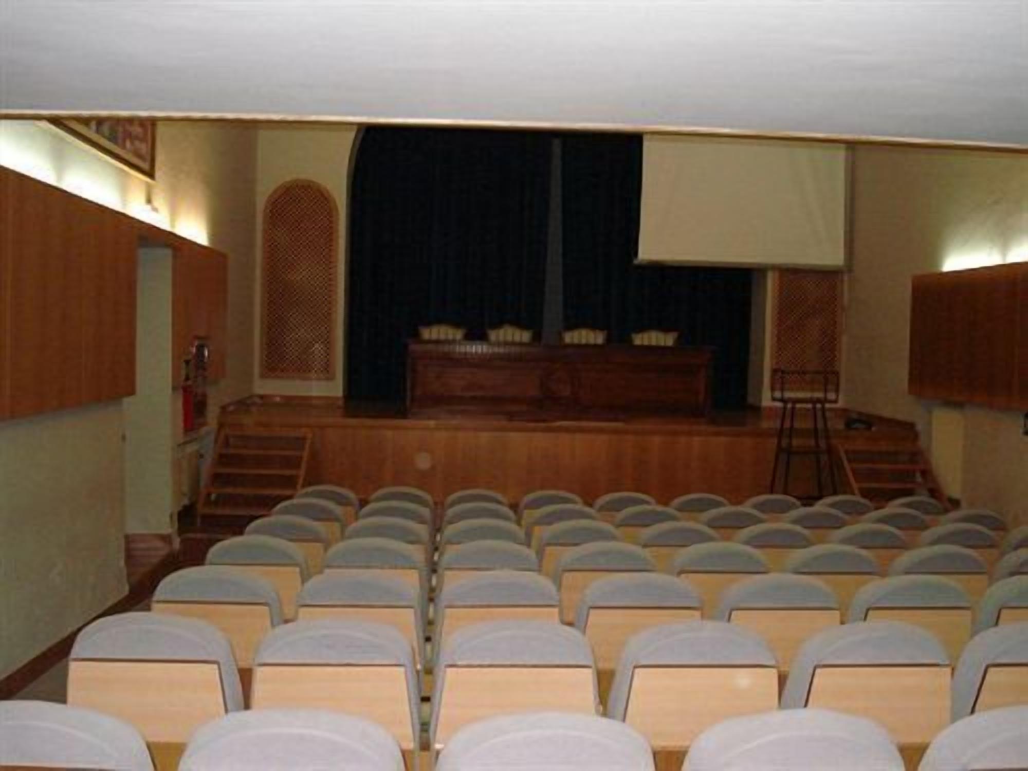 A theater with rows of seats, a stage with a curtain, and a wooden paneling wall.