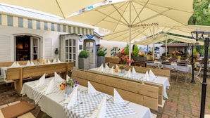 An outdoor dining area with wooden benches and tables, covered by large umbrellas. - Weichandhof (Munich)