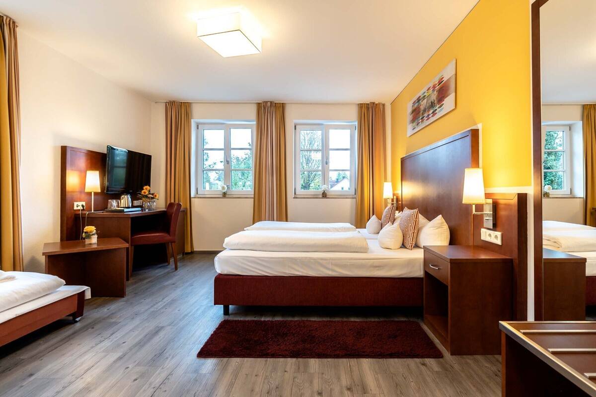 Una camera d'albergo con un letto, una scrivania, una televisione e finestre.
