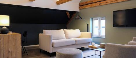 A modern living room with a sofa, ottoman, and chairs, a coffee table, a lamp, and a TV mounted on the wall.