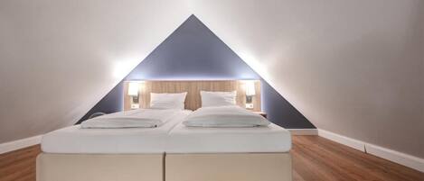 Un dormitorio con una cama centrada bajo un techo triangular, suelo de madera y un diseño moderno y sencillo.